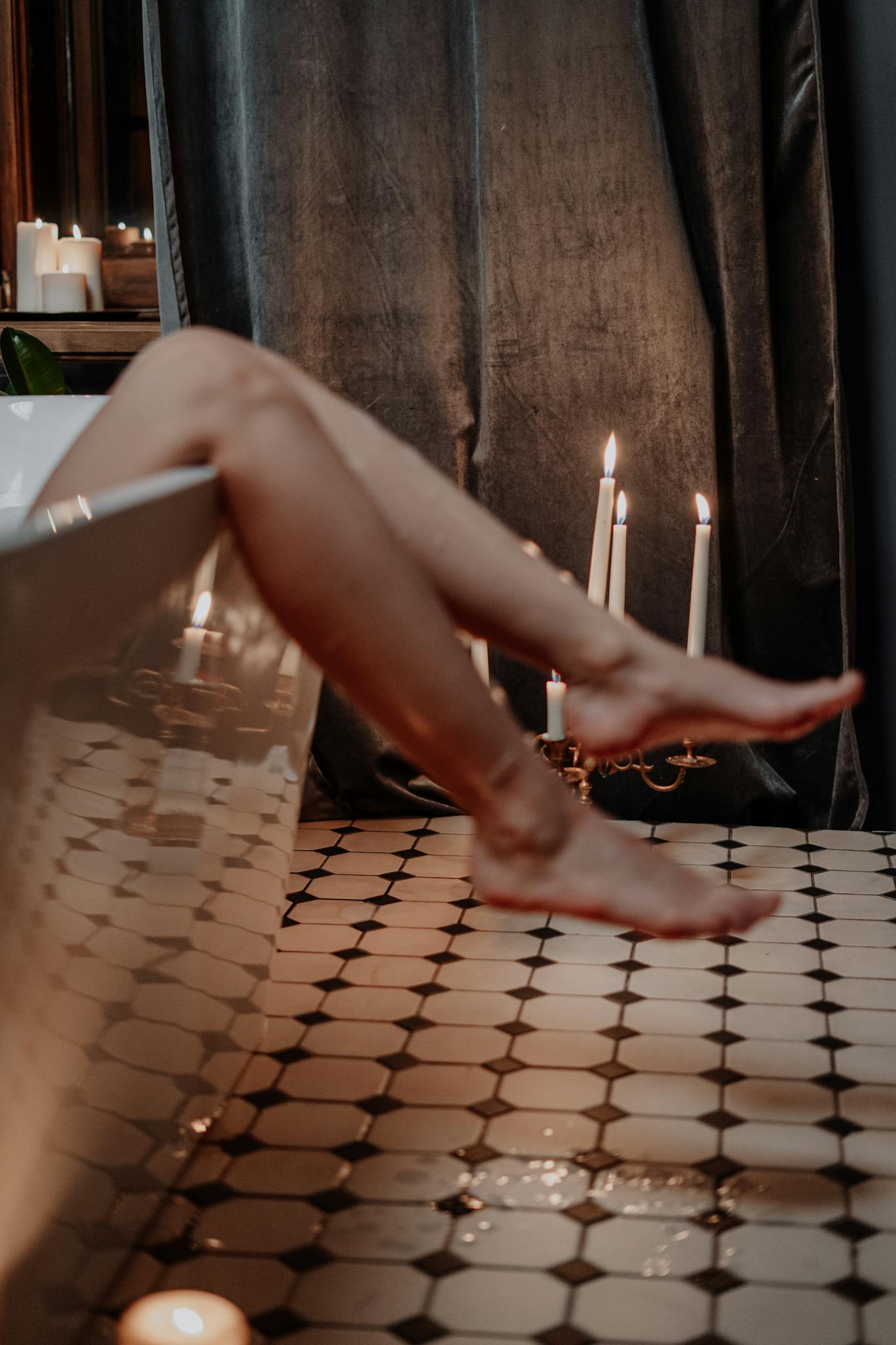 A serene setting with legs in a bathtub, surrounded by candles for a relaxing bath.